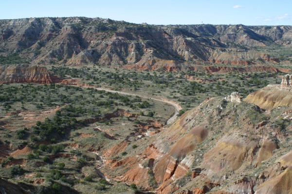 A broad canyon with riven sides, viewed from a high vantage point. The rock is banded red and a greenish colour
